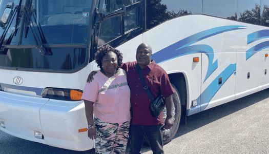 Husband and wife posing in front of their new motorchoach from Buses for Sale